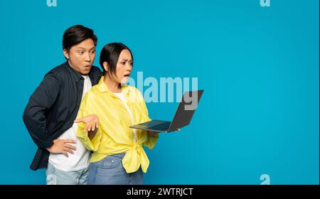 Shocked Asian couple looking at a laptop screen with surprised expressions Stock Photo
