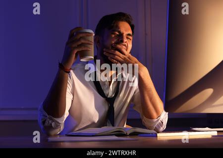 Tired man with coffee working late in office Stock Photo