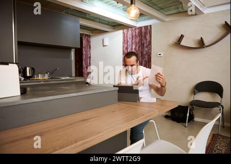 Male freelancer arguing during video conference, showing paper documents to his interlocutors during online meeting from home office. Stock Photo