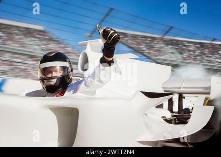 Race car driver in helmet giving a thumbsup from cockpit on racetrack. Stock Photo