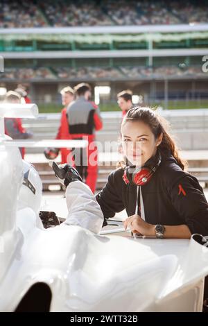 Young woman engineer with headphones around her neck working on a race car at the racetrack. Stock Photo