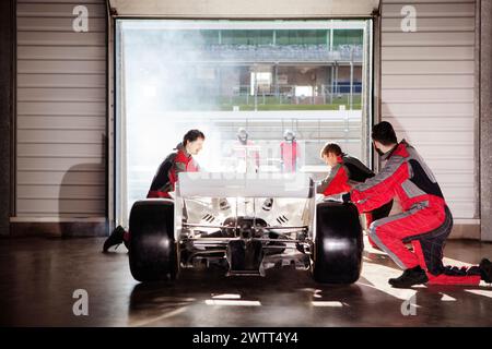 Pit crew team working on a race car in a garage against the backdrop of a sunlit track Stock Photo