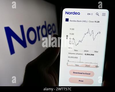 Person holding cellphone with webpage of Finnish financial services company Nordea Bank Abp in front of logo. Focus on center of phone display. Stock Photo