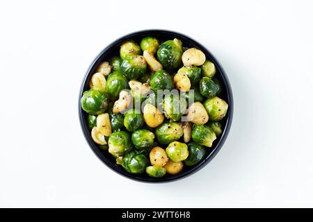 A bowl of roasted brussels sprouts and garlic cloves on a white background Stock Photo