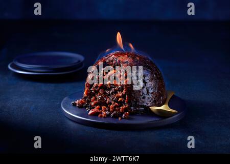 Flaming Christmas pudding on a festive table setting. Stock Photo