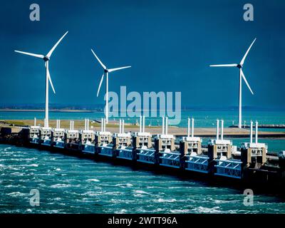 Wind turbines towering over a stormy seascape alongside a coastal barrier. Stock Photo