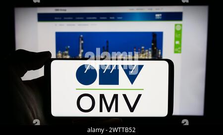 Person holding smartphone with logo of Austrian oil and gas company OMV Aktiengesellschaft in front of website. Focus on phone display. Stock Photo