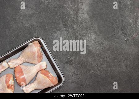 Chicken drumsticks in metal baking tray. Green branch of tomato on table. Black background. Copy space Stock Photo