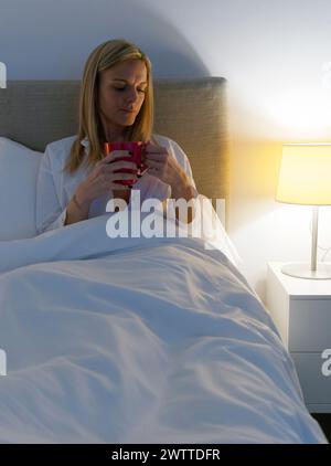 Serene morning moments as a woman enjoys her coffee in bed Stock Photo