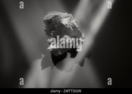 A crumpled piece of paper suspended in a void, with light casting dramatic shadows Stock Photo