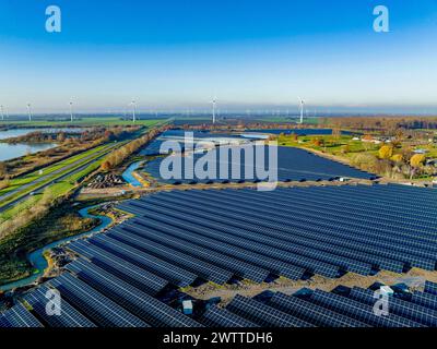 A vast solar farm sprawling under a clear blue sky flanked by wind turbines Stock Photo