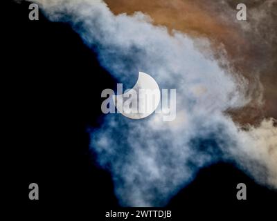 Partial solar eclipse peering through wispy clouds Stock Photo