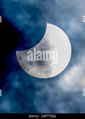 A partial solar eclipse veiled by wispy clouds against a deep blue sky. Stock Photo