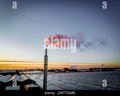 Smoke billowing from a chimney at dawn with a vibrant sunrise in the background Stock Photo