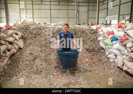 Worker smiling amidst a mountain of plastic bottle caps for recycling, plastic recycling factory, Thailand Stock Photo