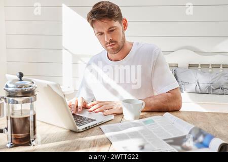 Man working on laptop at a sunny home table Stock Photo