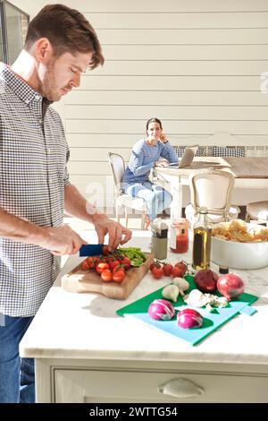 Man chopping vegetables in a kitchen with woman in background Stock Photo