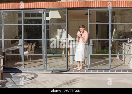 Man in a towel drinking coffee by glass doors. Stock Photo