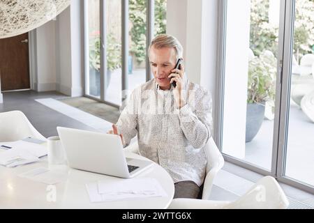 Man talking on phone while working on a laptop at a bright office Stock Photo