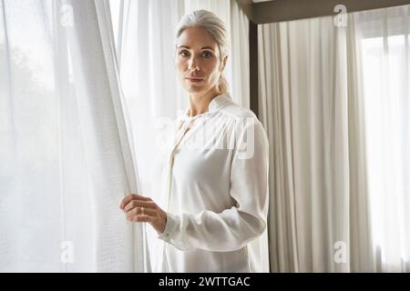 Woman standing by the window with curtains. Stock Photo