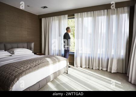 Man standing by the window in a bedroom Stock Photo