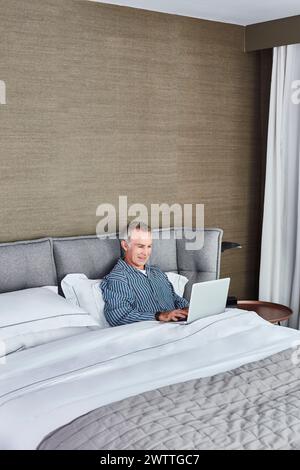 Man using laptop while sitting in bed Stock Photo