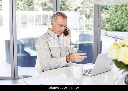 Man talking on phone while working on laptop at home Stock Photo