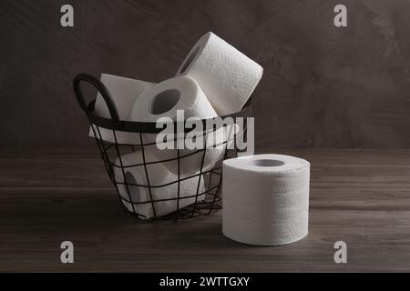 Soft toilet paper rolls in metal basket on wooden table Stock Photo