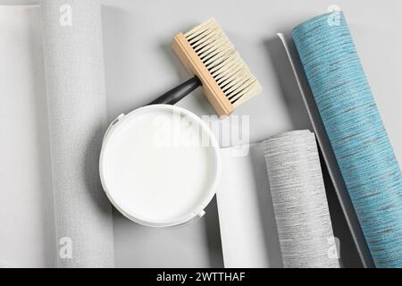 Different wallpaper rolls, brush and bucket with glue on light background, flat lay Stock Photo
