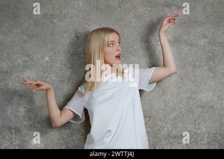 Woman posing with surprised expression against a gray wall Stock Photo