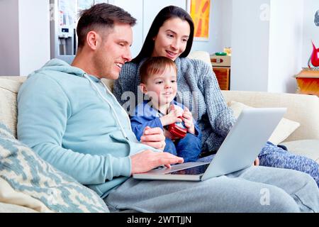 Family with toddler using a laptop on a sofa Stock Photo