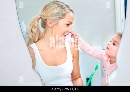 Toddler brushing mother's teeth in bathroom Stock Photo