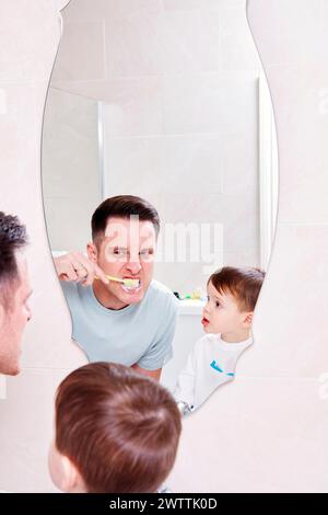 Man and child brushing teeth together in mirror reflection Stock Photo