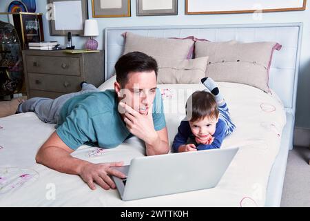 Man and child using laptop on bed Stock Photo