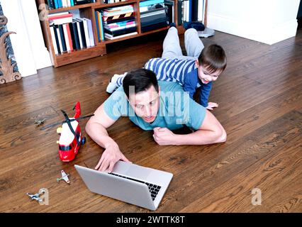 Man working on laptop with child playing behind him Stock Photo