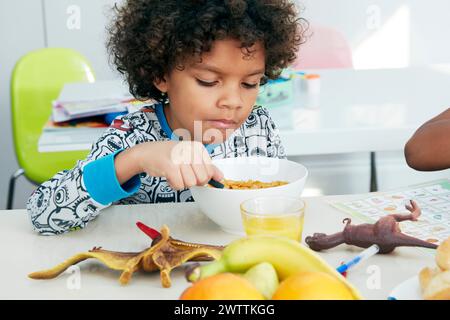 Child eating breakfast with toys on table. Stock Photo