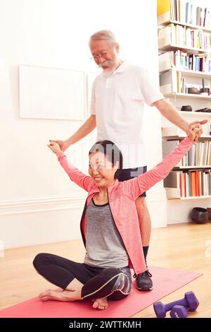 Senior man assisting a woman in a yoga pose Stock Photo