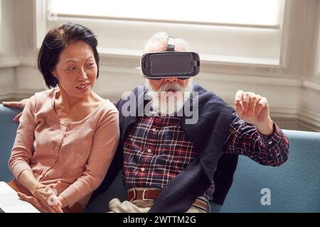 Elderly man trying on VR headset, woman watching Stock Photo