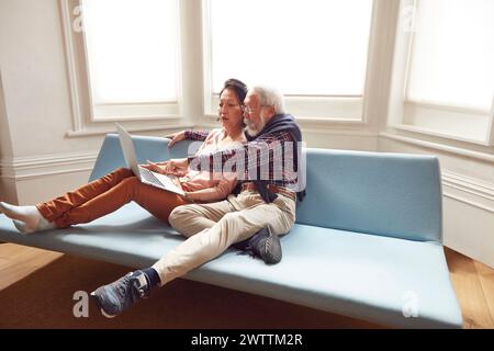 Elderly couple using a laptop on a blue sofa Stock Photo