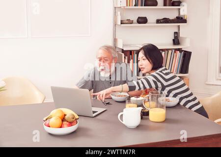 Two people using a laptop at a dining table. Stock Photo