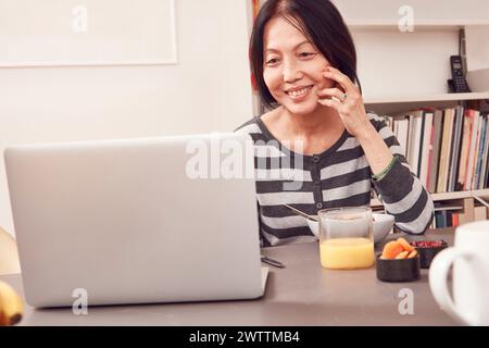 Woman smiling at a laptop on a desk with snacks Stock Photo