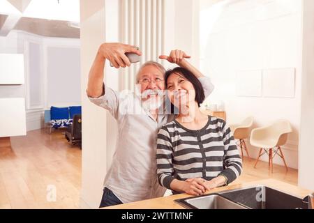 Elderly couple taking a selfie in a bright kitchen. Stock Photo