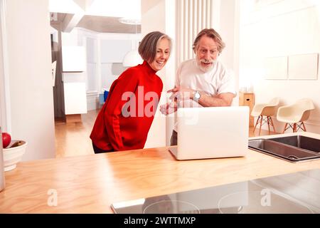 Mature couple excitedly looking at a laptop screen in a kitchen. Stock Photo
