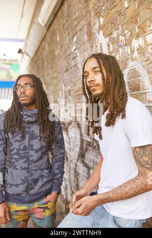 Two men with dreadlocks standing by a graffiti wall Stock Photo