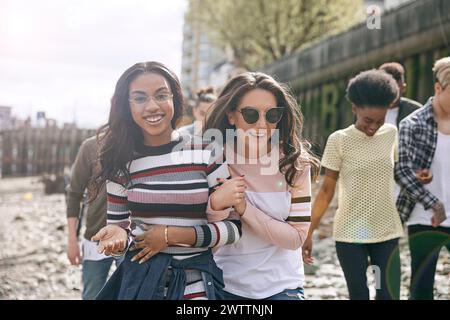 Two women smiling and walking outdoors with friends in the background. Stock Photo