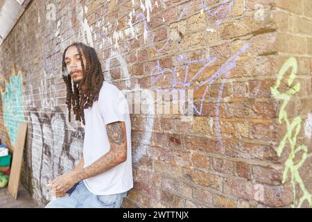 Man leaning against a graffiti-covered wall Stock Photo