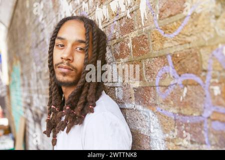 Man with dreadlocks against a graffiti wall Stock Photo