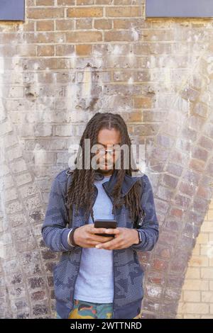 Man using smartphone against brick wall Stock Photo