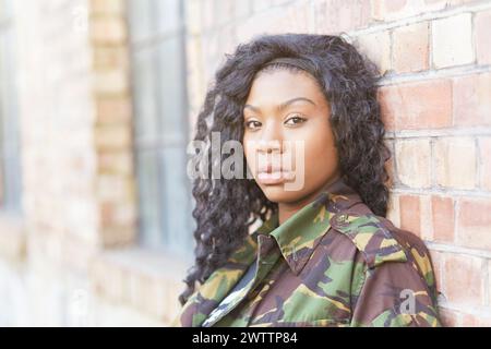 Woman in camouflage leaning against a brick wall Stock Photo