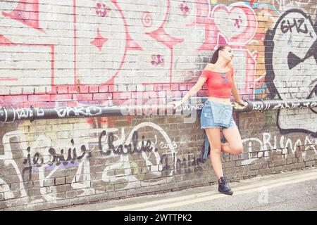 Young woman leaning against a graffiti-covered wall Stock Photo